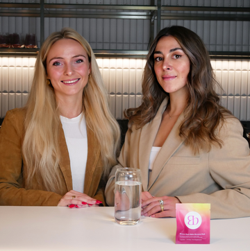 Bloma founders smiling at the camera with a glass of water and the Blōma Recovery Pack displayed on the table, a powerful duo behind a wellness brand designed for women, by women.