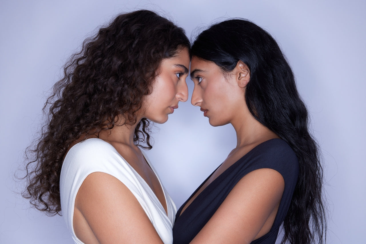 Two women standing face to face in a powerful, intimate pose, symbolizing strength, connection, and feminine energy, with soft lighting and minimal background.