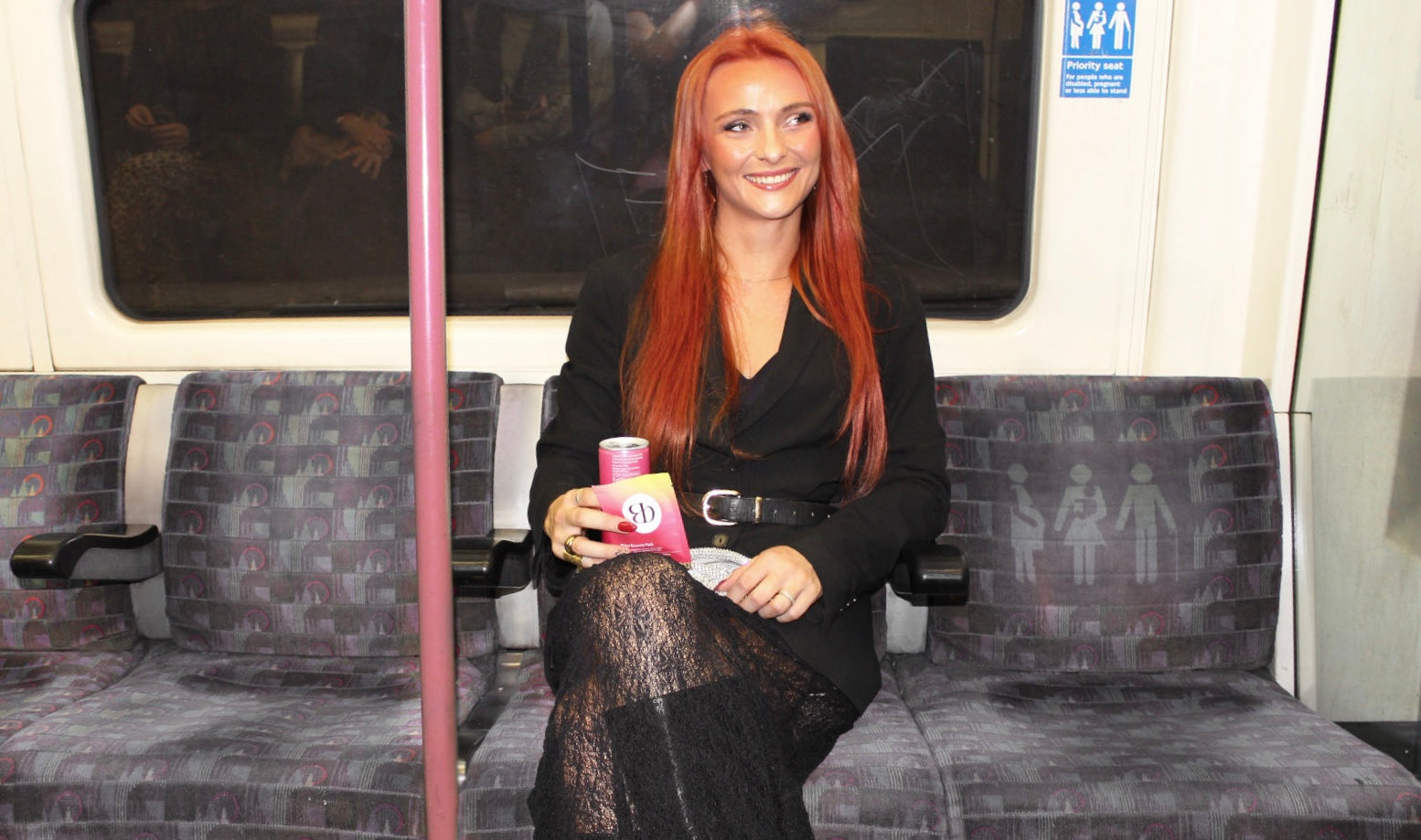 Smiling woman holding gin in a can and a Blōma Recovery Pack in the london tube, ready for a big night out as a party girl and not be hungover tomorrowslider_item_KrFVfA